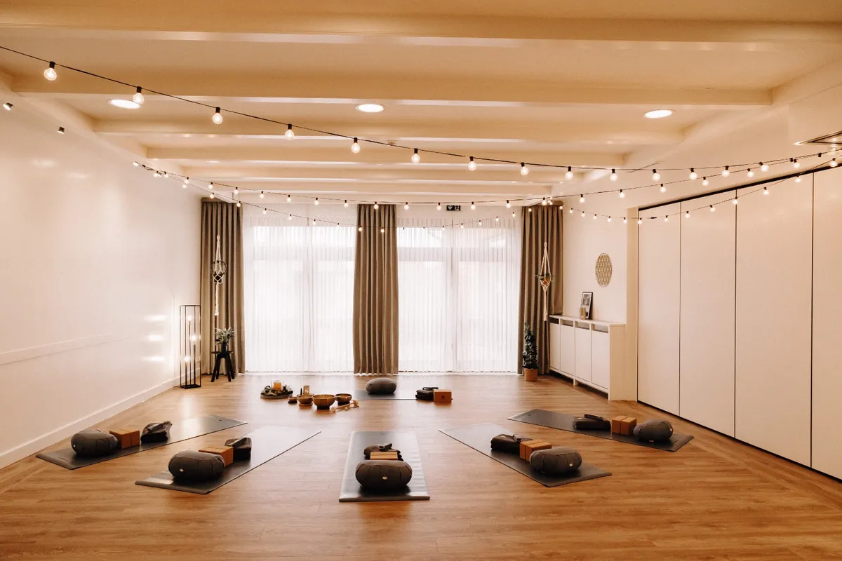 Heller Yogaraum mit ausgelegten Matten, Meditationskissen und Lichterketten
