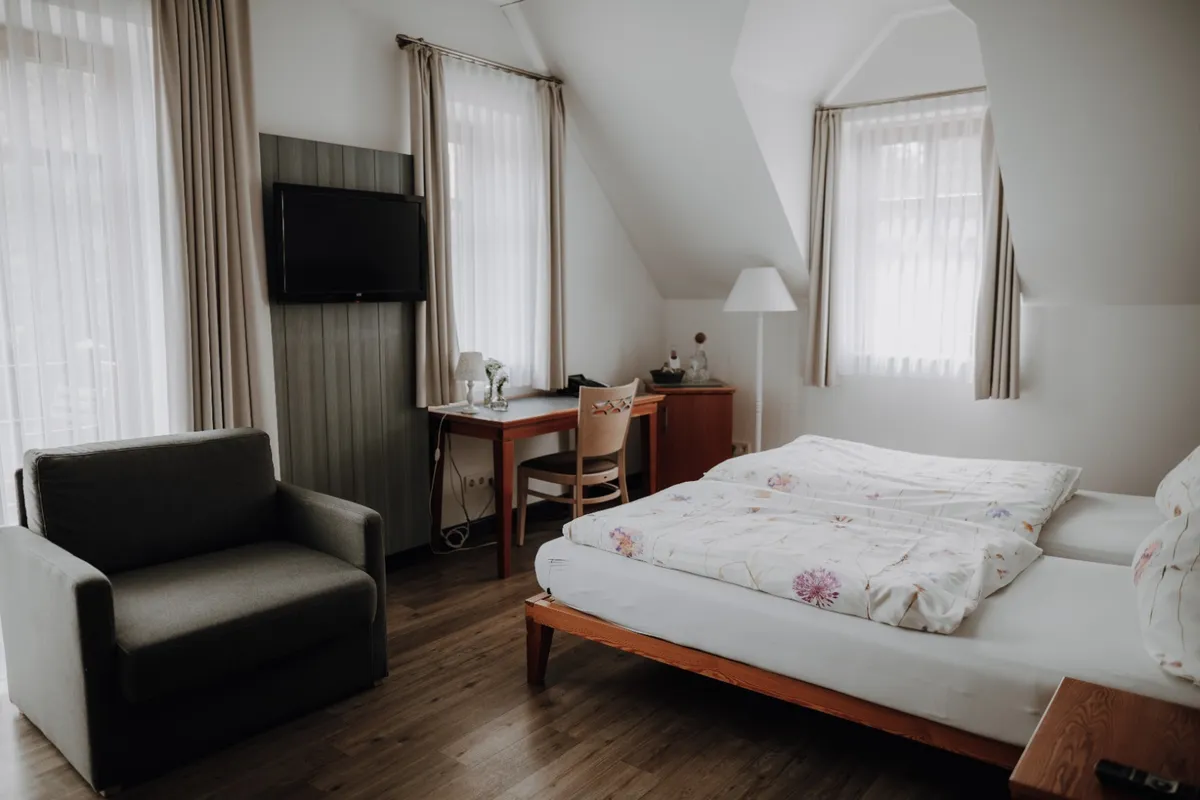 Helles Hotelzimmer im Okelmann's mit Doppelbett, Sessel und Schreibtisch