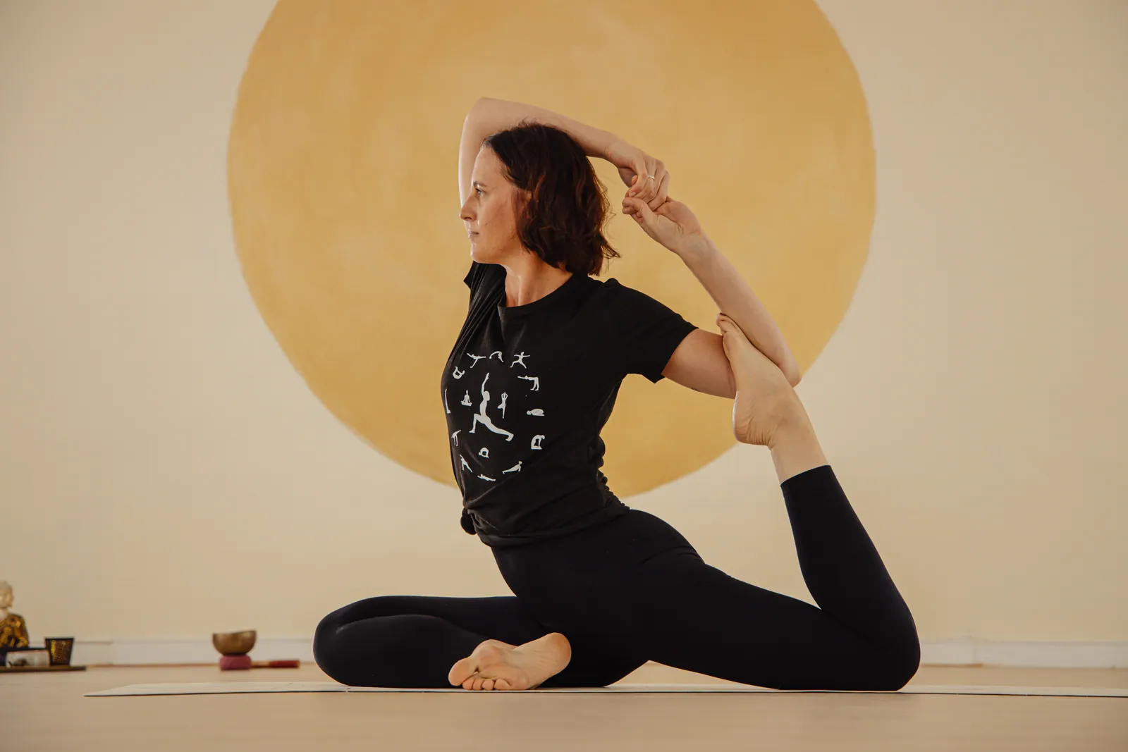 Janina in einer Yogahaltung auf der Matte, vor einem großen, warm gemalten goldenen Kreis.